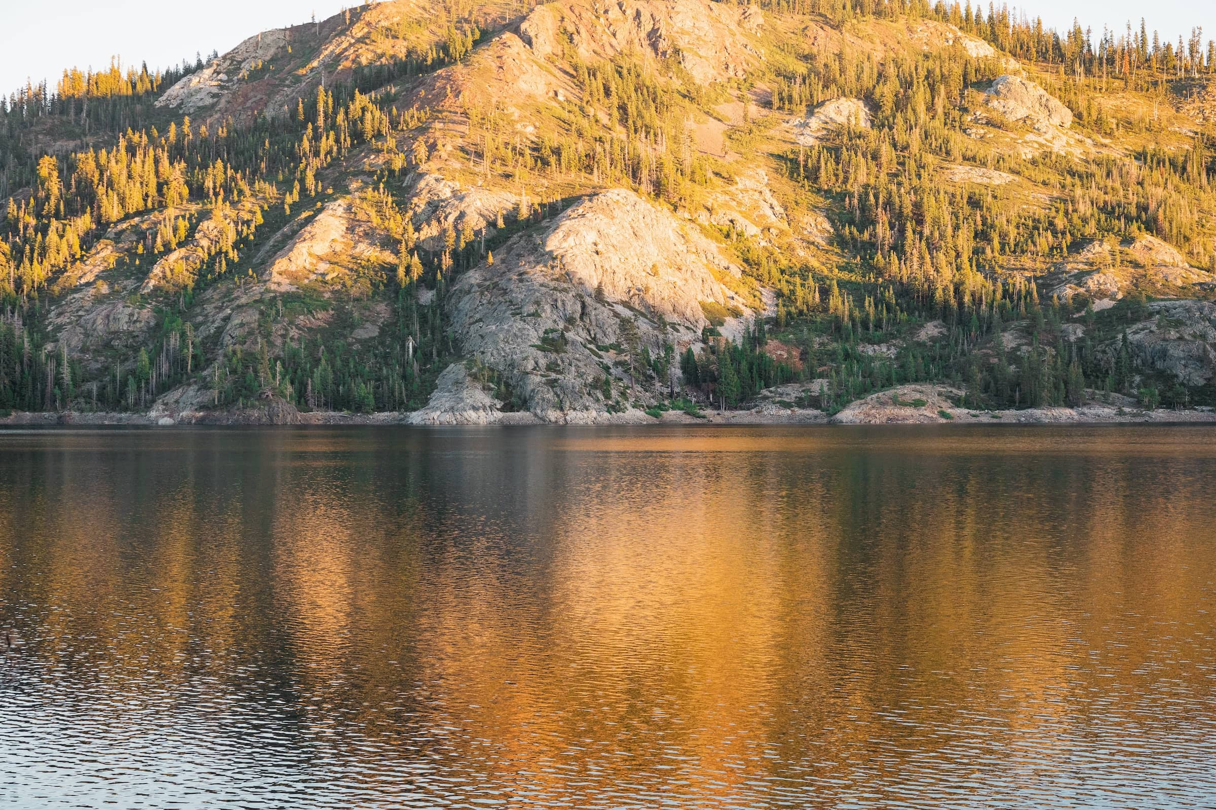 A 50/50 photo of a lake and a mountainous shoreline zoomed in to the distance creating a contrast between the two, with golden light enveloping all.