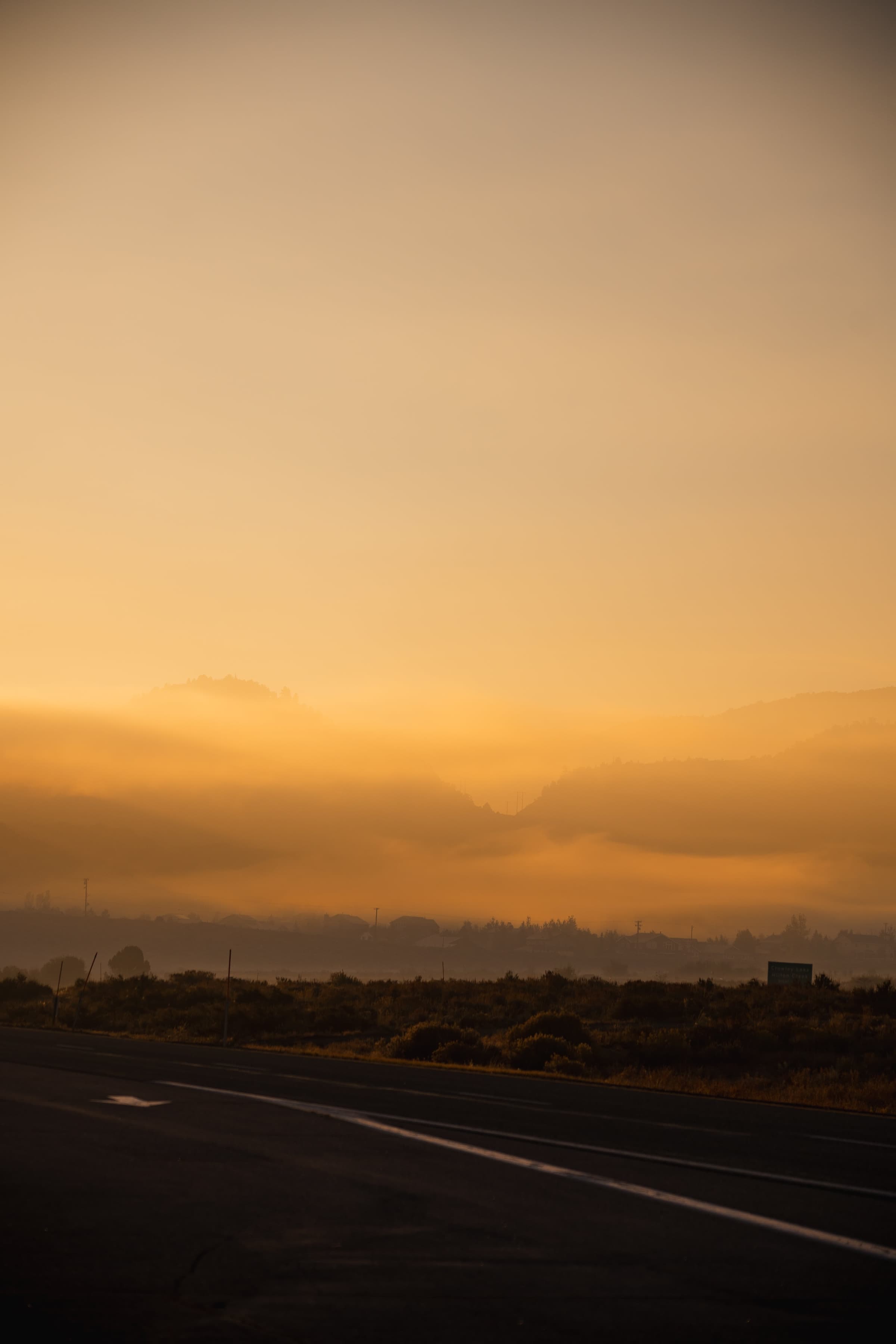 A serene landscape at sunrise with a road leading towards mist-enshrouded hills under a gradient orange sky.